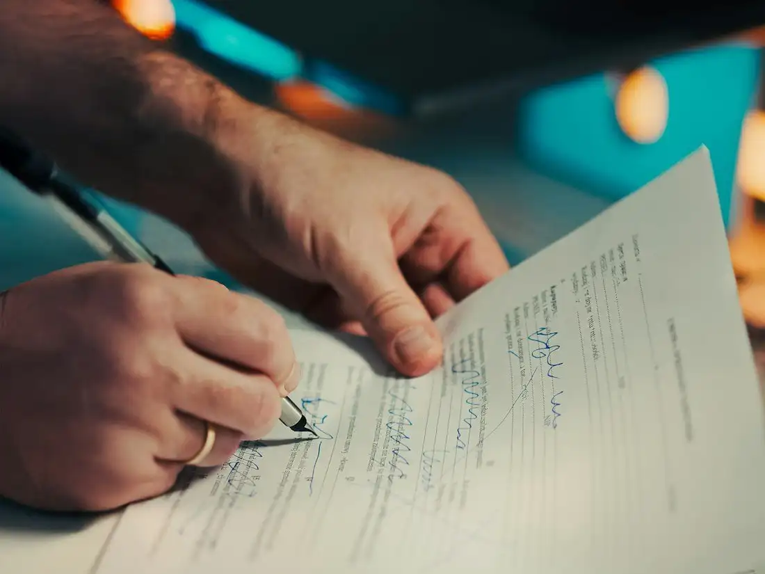 A hand signing a form with a ballpoint pen