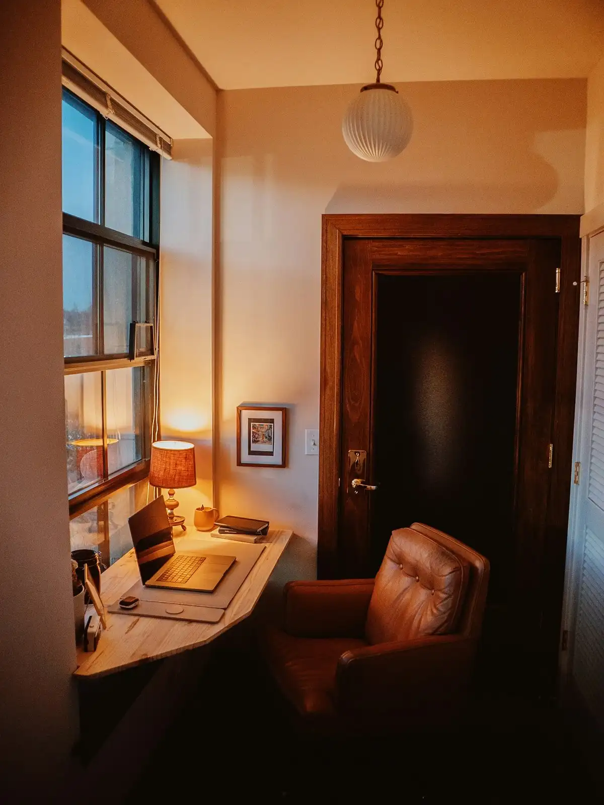 A small office with a desk by the window, a lamp and a leather armchair