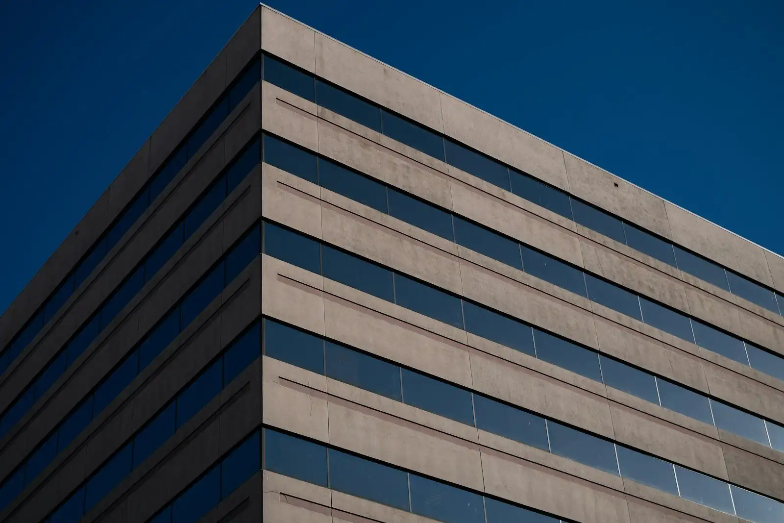 The upper floors of a tan office building against a deep blue sky